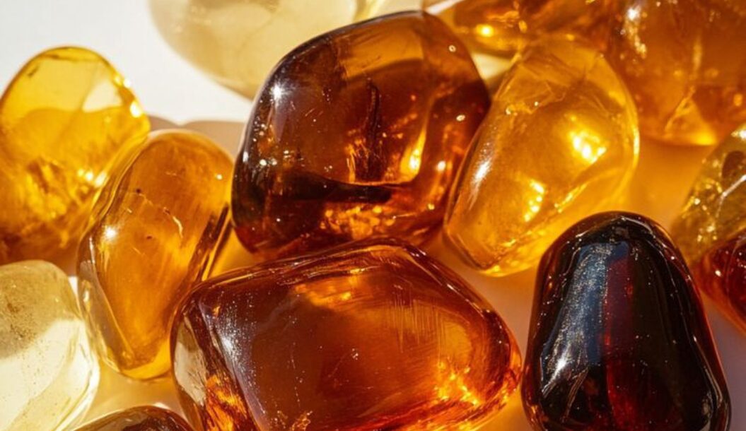 A variety of polished amber stones in different shades of yellow and brown, scattered on a light surface.