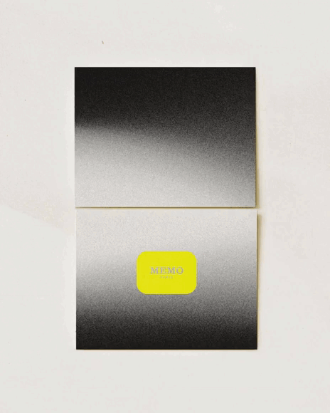 A folded memo pad with a gradient black and white cover and a bright yellow label that reads "MEMO" in the center.