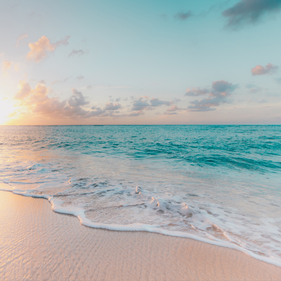 A serene beach scene at sunset, showcasing soft waves lapping against a sandy shore, with a gradient sky of pastel colors.