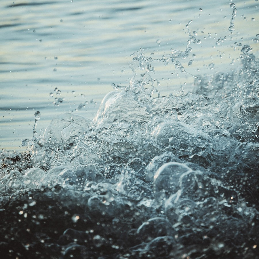 Close-up of water splashing and creating bubbles, with a calm, reflective surface in the background.