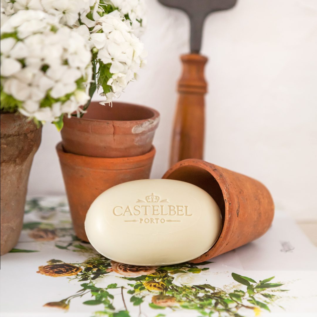 A clay pot tipped over with a CASTELBEL Porto soap inside, surrounded by smaller clay pots and a floral arrangement.