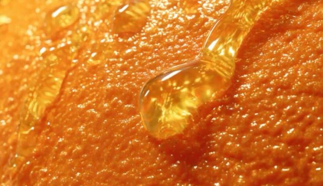 Close-up image of an orange's textured surface, with droplets of juice glistening on it.