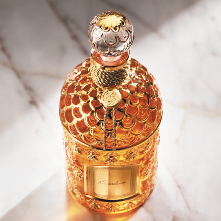 A luxurious, ornate bottle of perfume with a golden, textured design and intricate top, set against a marble surface.