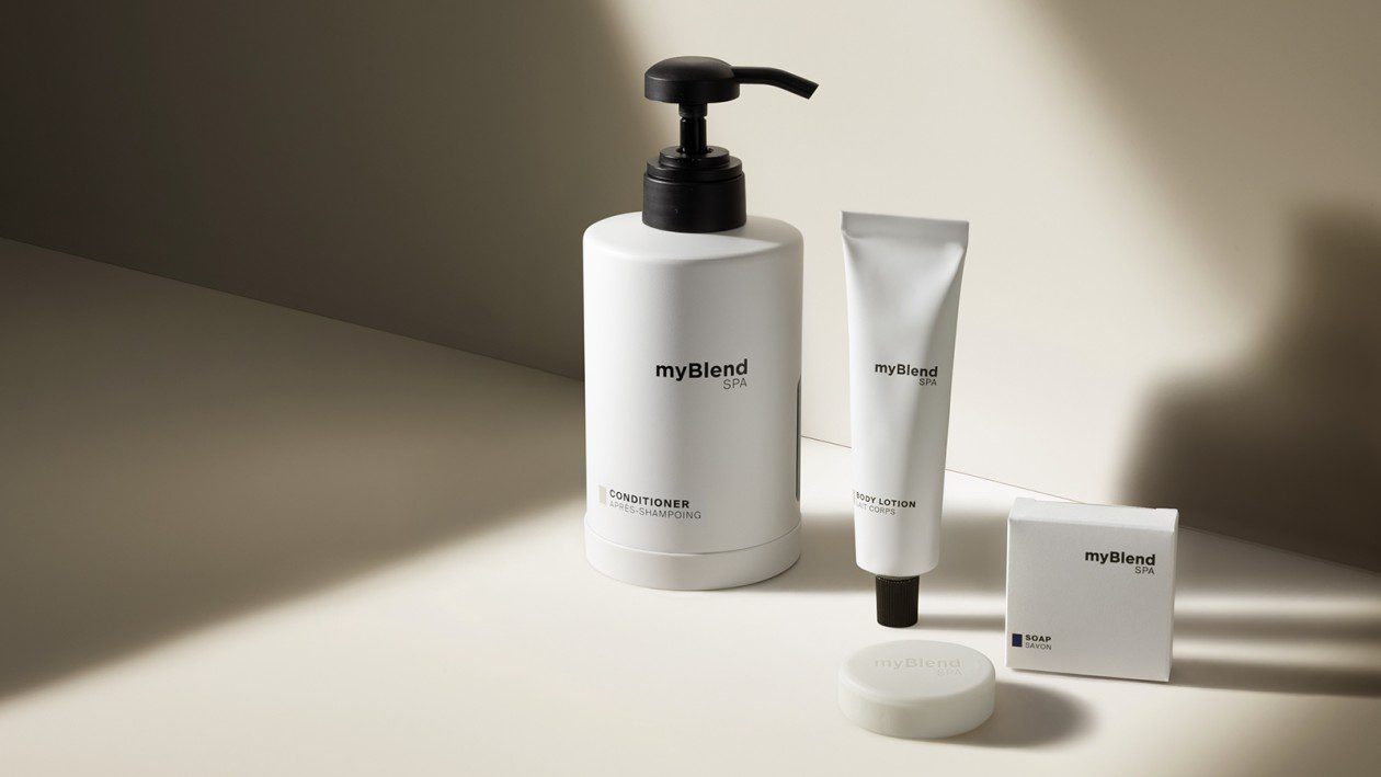 A minimalist arrangement of myBlend SPA products including conditioner, body lotion, and soap, displayed in white packaging with soft natural light and shadows on a neutral background.