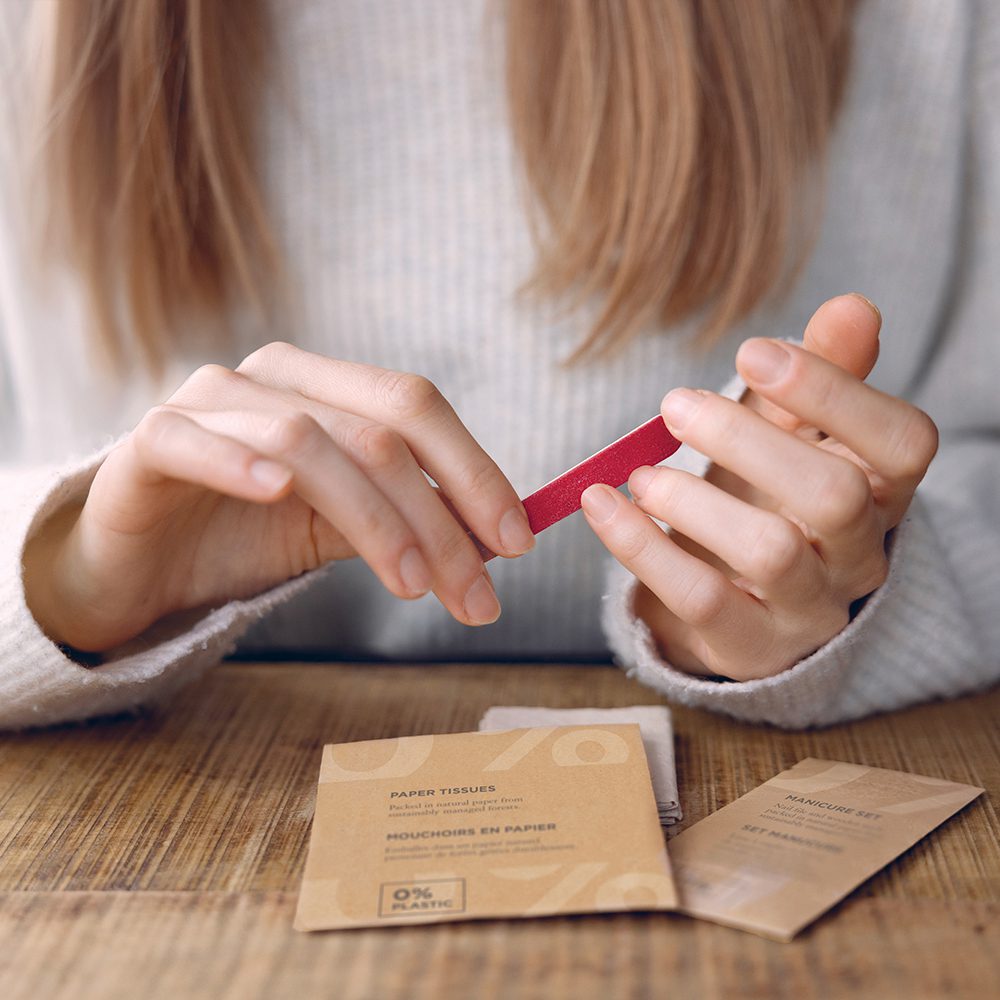 A person is holding a small red paper tissue while sitting at a wooden table, with a package of paper tissues visible nearby.