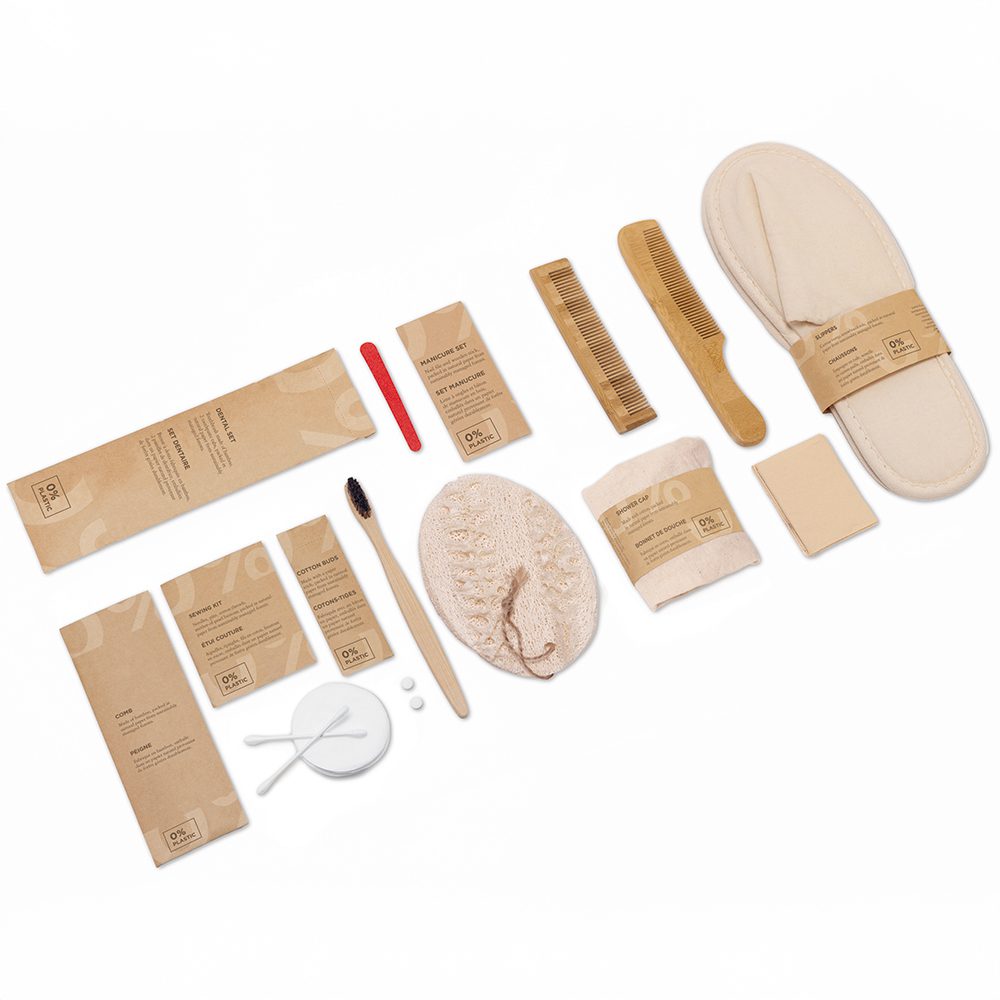 A neatly arranged set of eco-friendly personal care items, including a toothbrush, comb, slippers, facial sponge, and packaging made from natural materials, laid out on a white background.