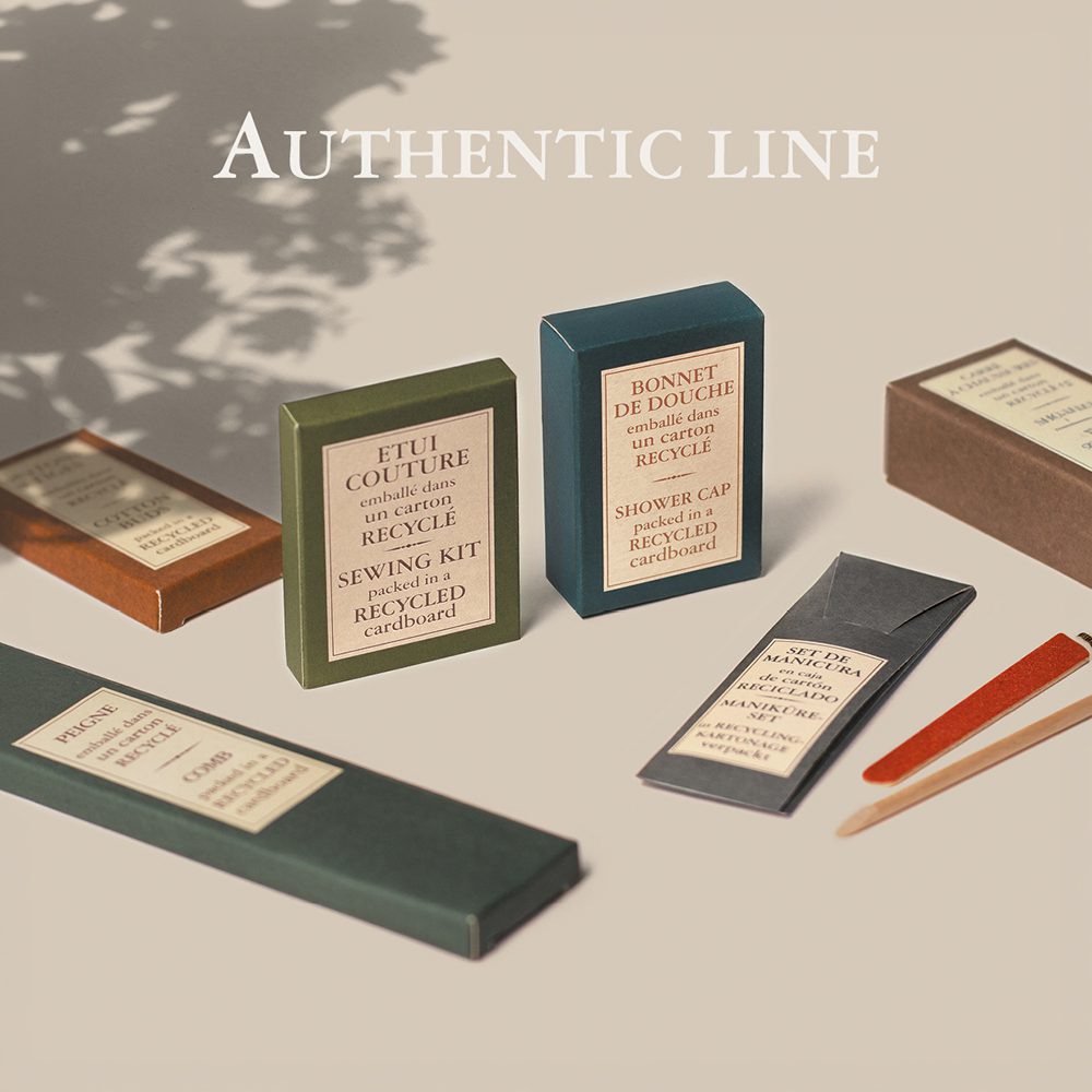 A collection of eco-friendly packaging for various personal care items, including a sewing kit, shower cap, and manicure tools, all labeled as made from recycled cardboard. The products are arranged aesthetically on a neutral background with the words "Authentic Line" displayed above.