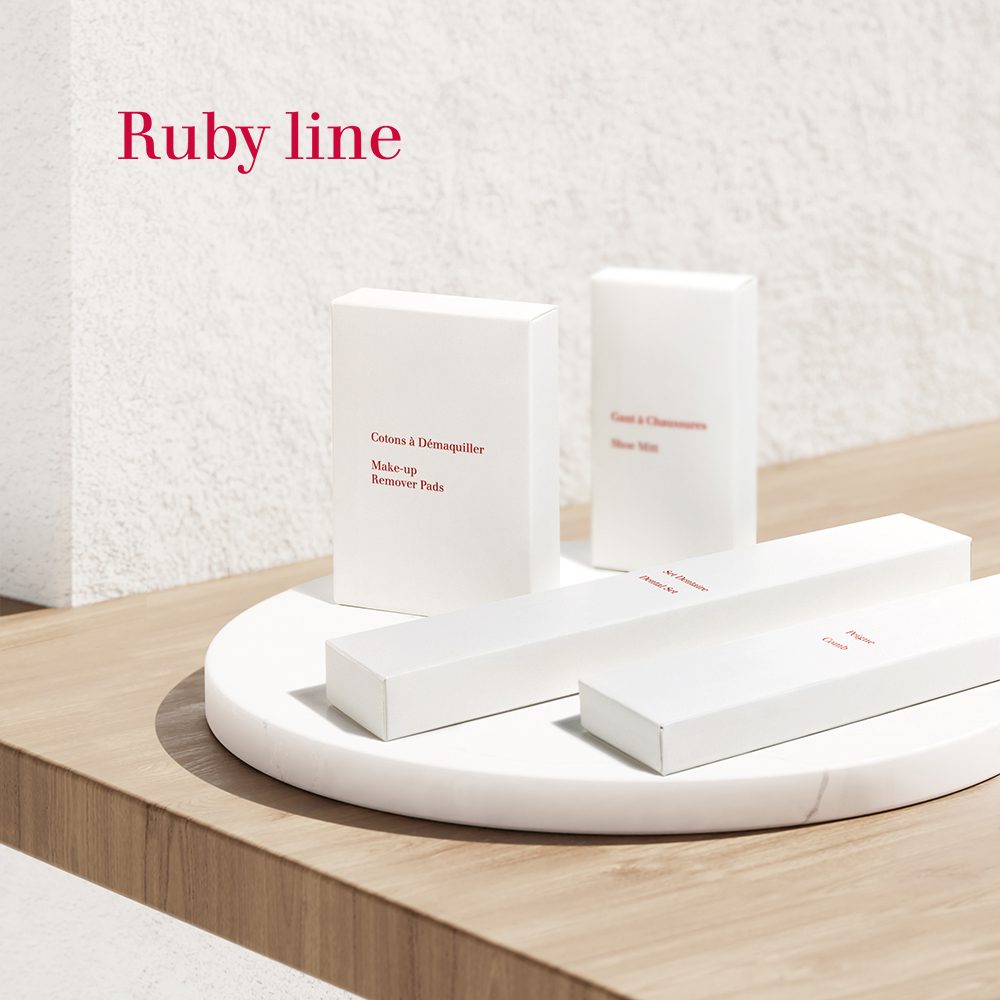 A minimalist display of white product boxes labeled "Ruby line," including makeup remover pads and cleansing wipes, arranged on a round wooden surface against a light backdrop.