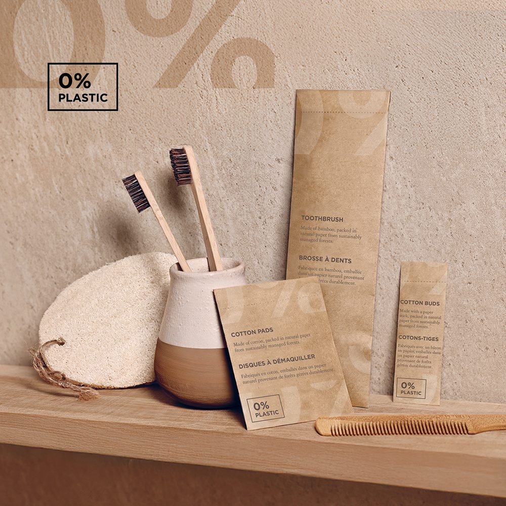 A minimalist bathroom shelf displaying eco-friendly personal care products, including a bamboo toothbrush, cotton pads, cotton buds, and a natural sponge, all packaged in recyclable materials with a "0% plastic" label.