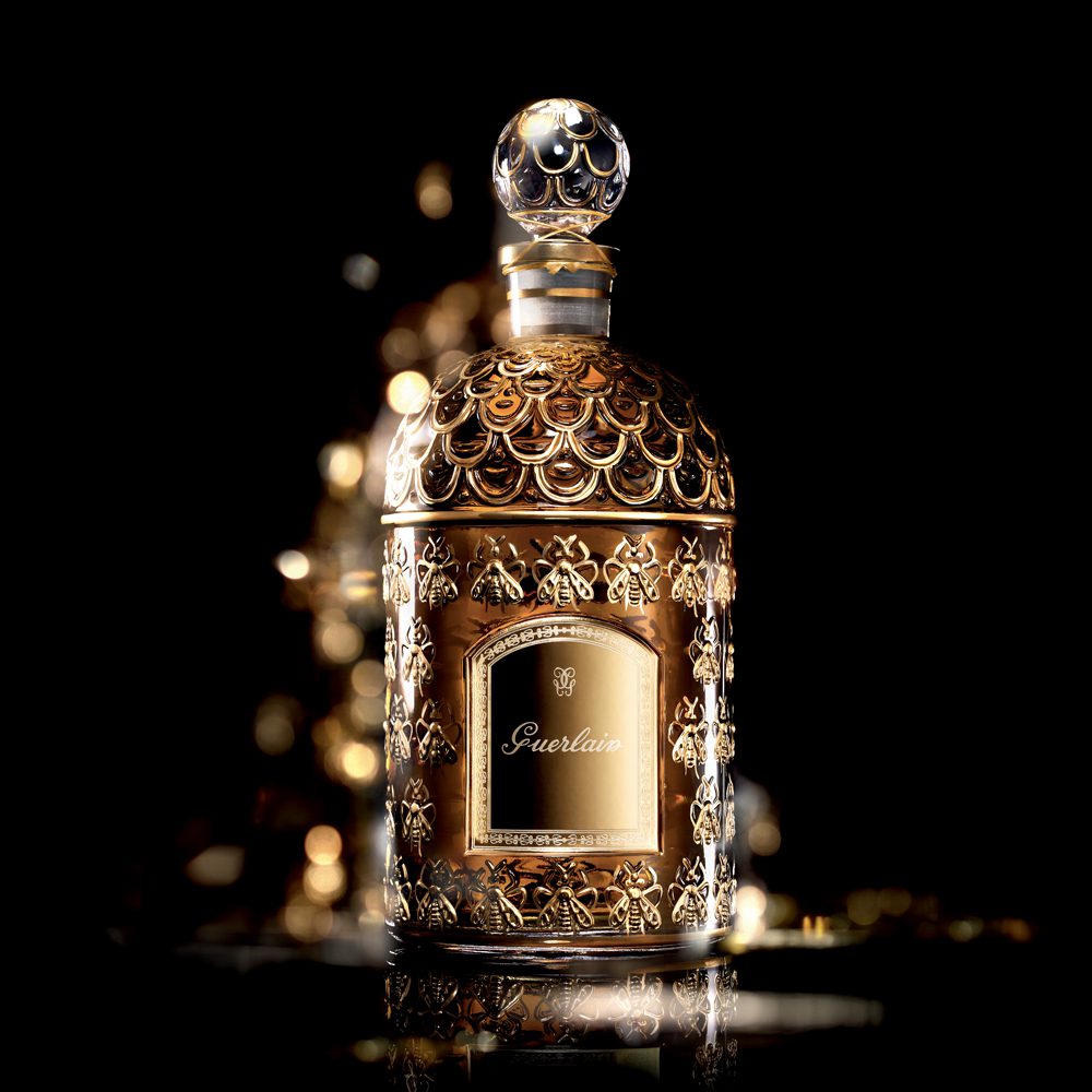 A luxurious golden perfume bottle with intricate detailing and a decorative cap, illuminated against a dark background.