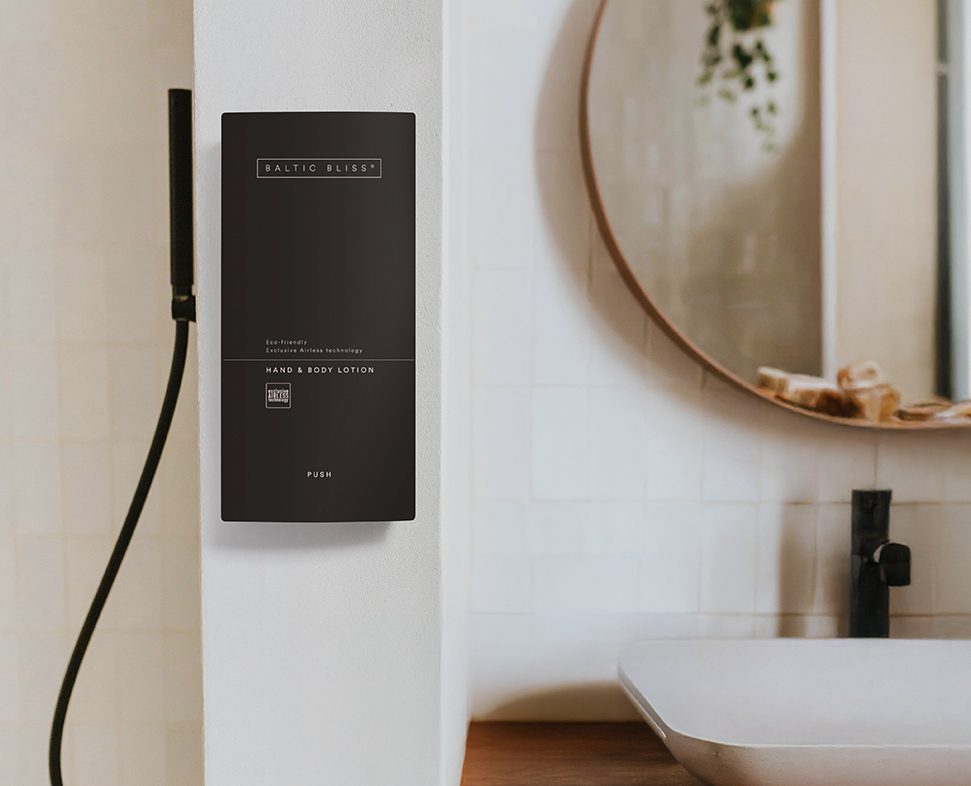A sleek black lotion dispenser labeled "BALTIC BLISS" mounted on a white wall next to a modern sink and faucet in a bathroom setting.