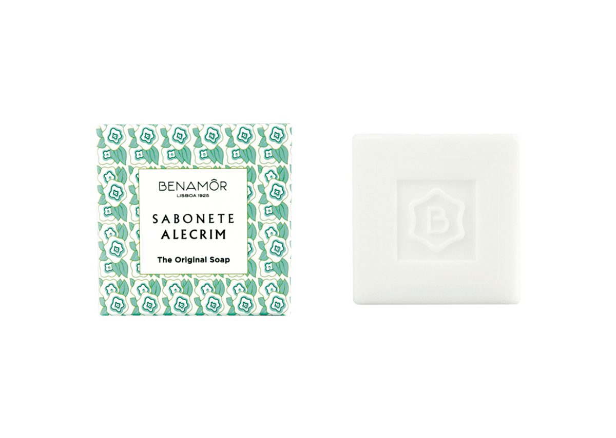 A square bar of white soap beside its patterned packaging featuring green, blue, and white designs with the text "BENAMÓR Sabonete Alecrim" and "The Original Soap."