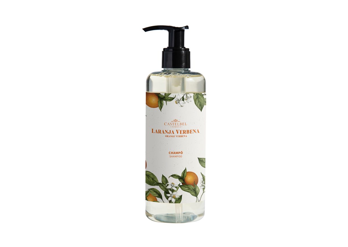 A clear plastic bottle of shampoo labeled "Laranja Verbena," featuring a decorative design with orange and white floral elements. The bottle has a black pump dispenser on top.