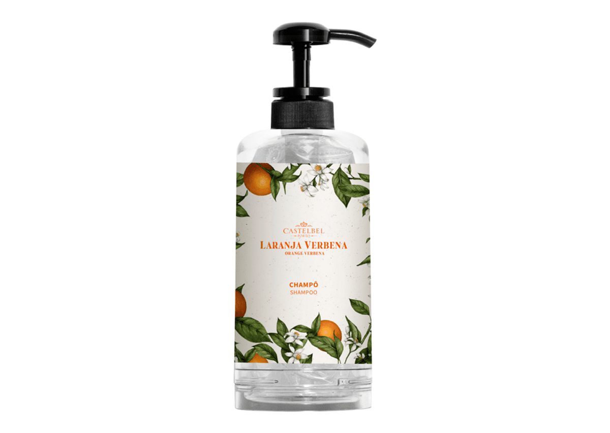 A clear shampoo bottle with a pump dispenser, featuring a decorative label adorned with orange fruits and green leaves, labeled "Laranja Verbena."