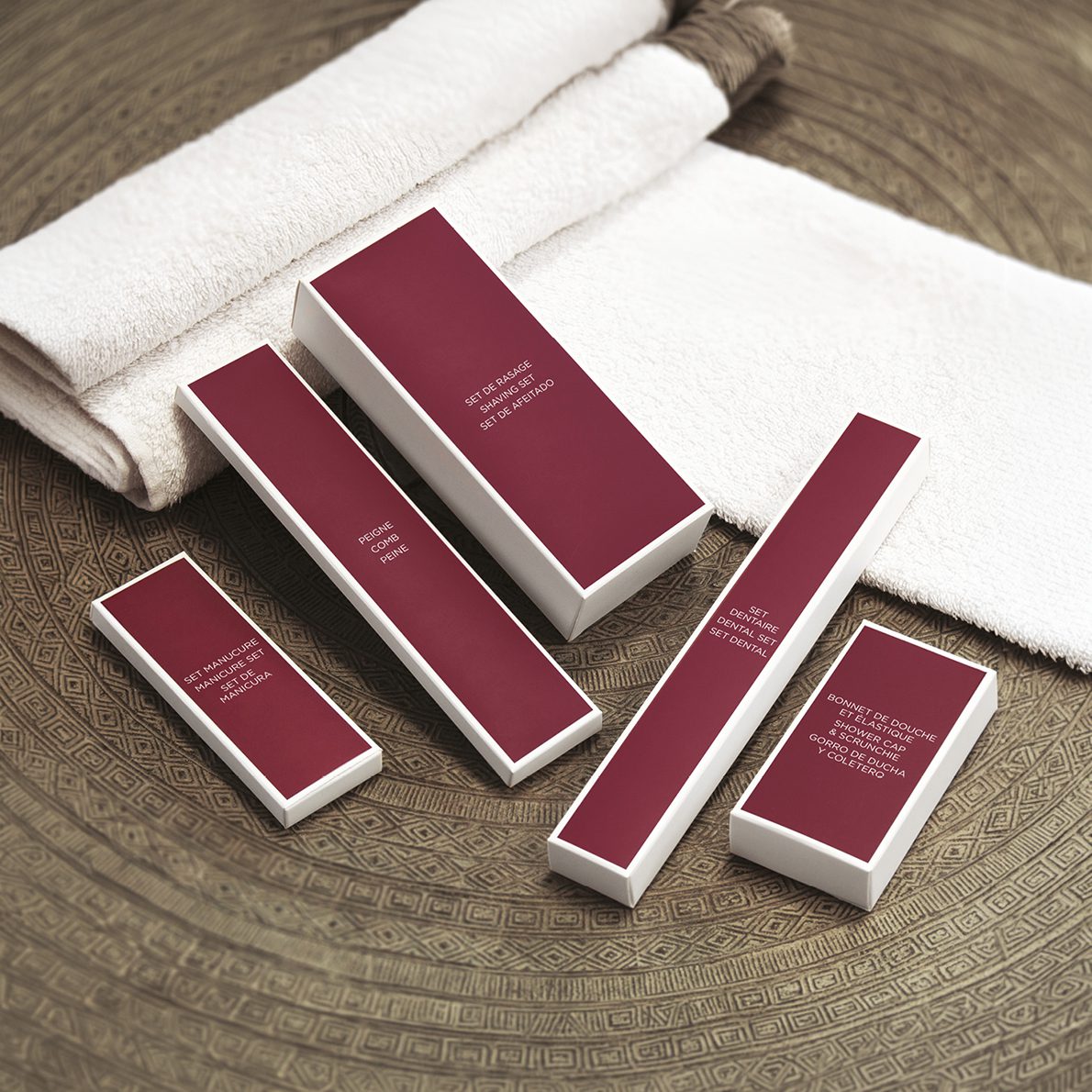 A collection of elegant skin care product boxes in burgundy and white, arranged on a textured, circular surface next to a stack of soft white towels.