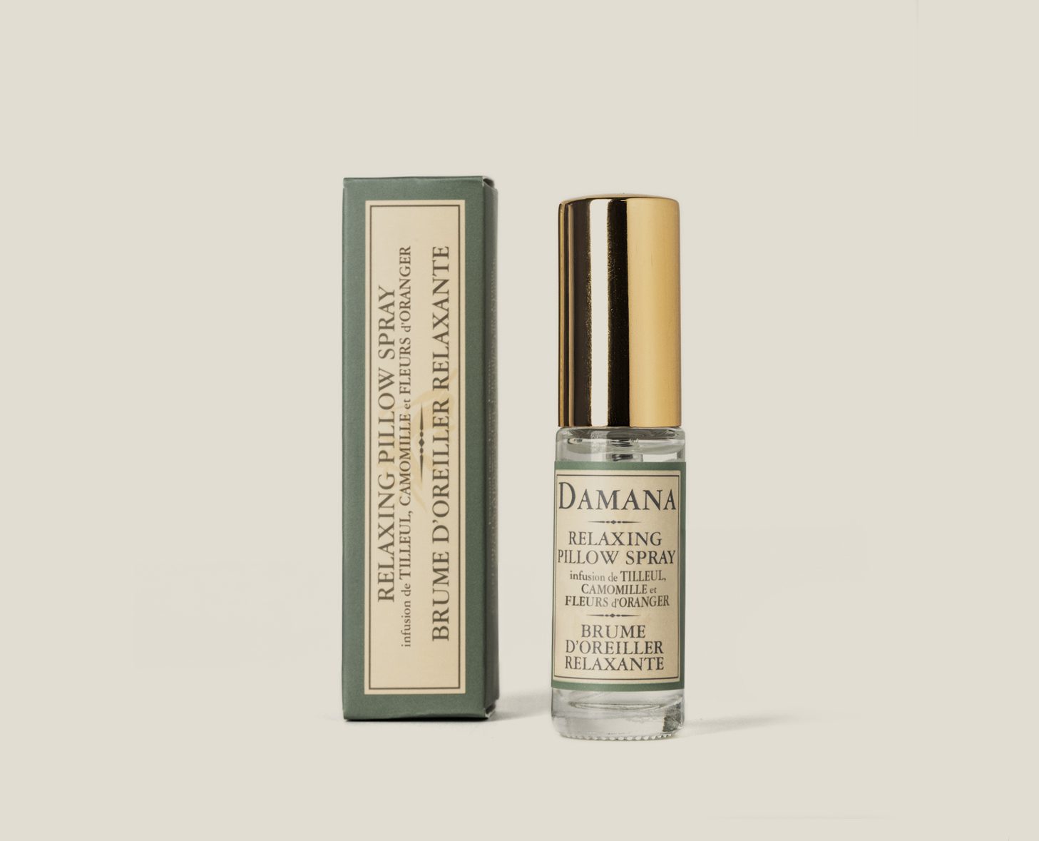A small glass bottle of Damana Relaxing Pillow Spray with a gold cap, next to its green and cream box packaging. The label features text in both English and French, detailing its soothing properties.