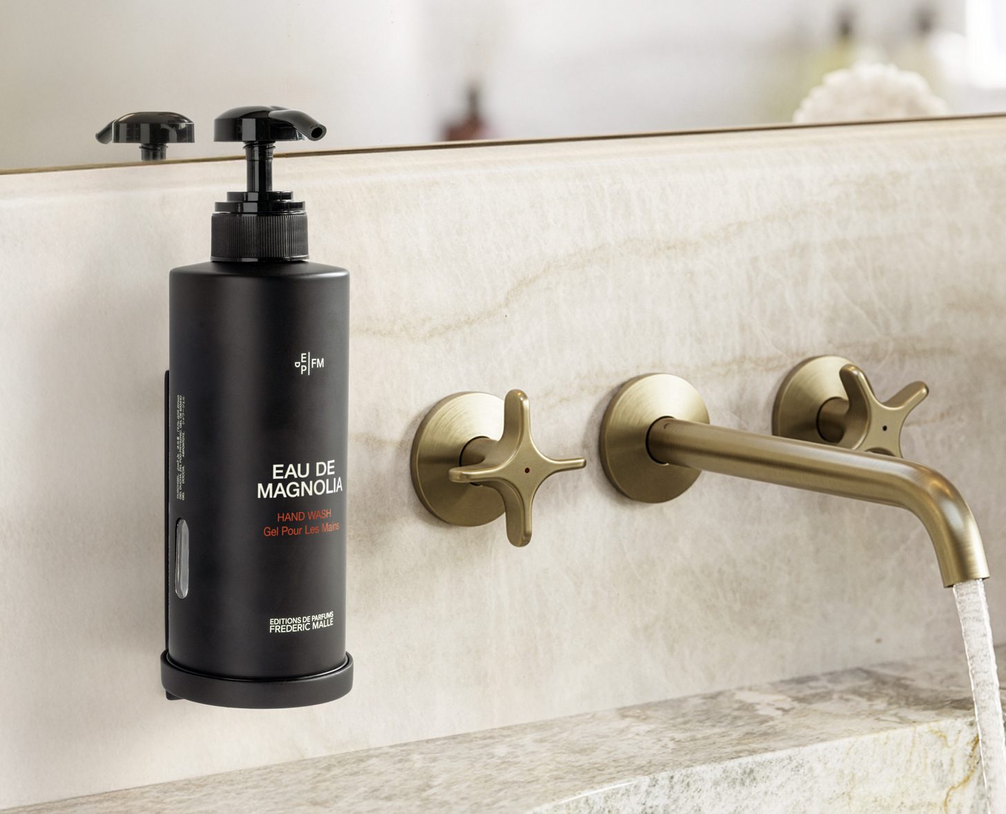 A black cylindrical pump bottle labeled "Eau de Magnolia" is mounted on a marble sink with stylish brass taps in a modern bathroom setting.