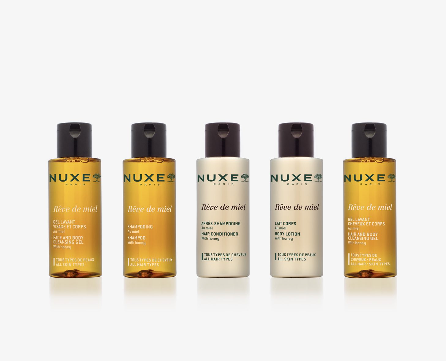 A collection of five NUXE Rêve de Miel hair and body care products, including shampoo, conditioner, and body lotion, displayed in a neat row. Each product features amber-colored bottles with white labels.