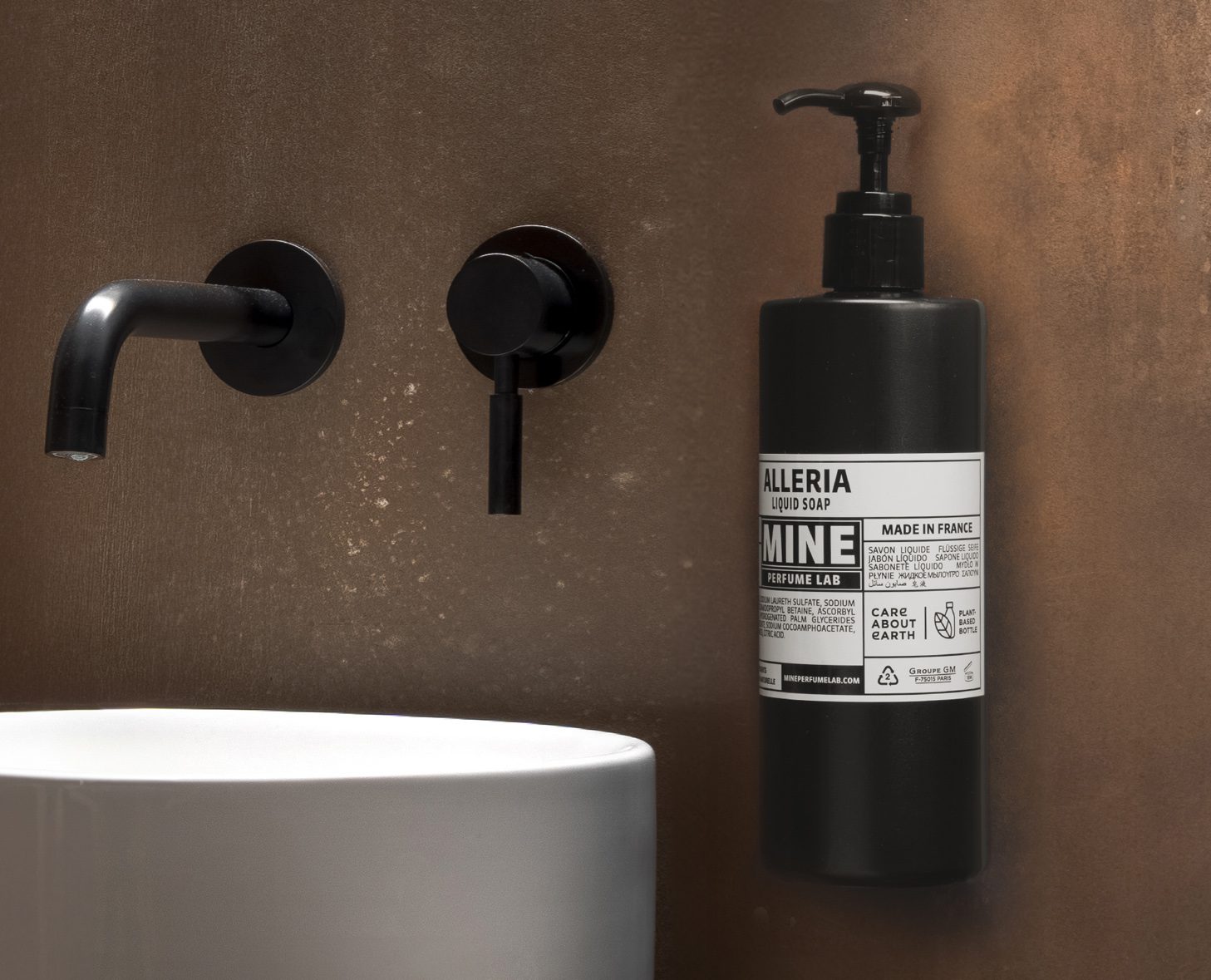 A stylish bathroom setting featuring a black liquid soap dispenser labeled "Alleria" mounted on a textured wall, alongside sleek black faucets and a white round sink.