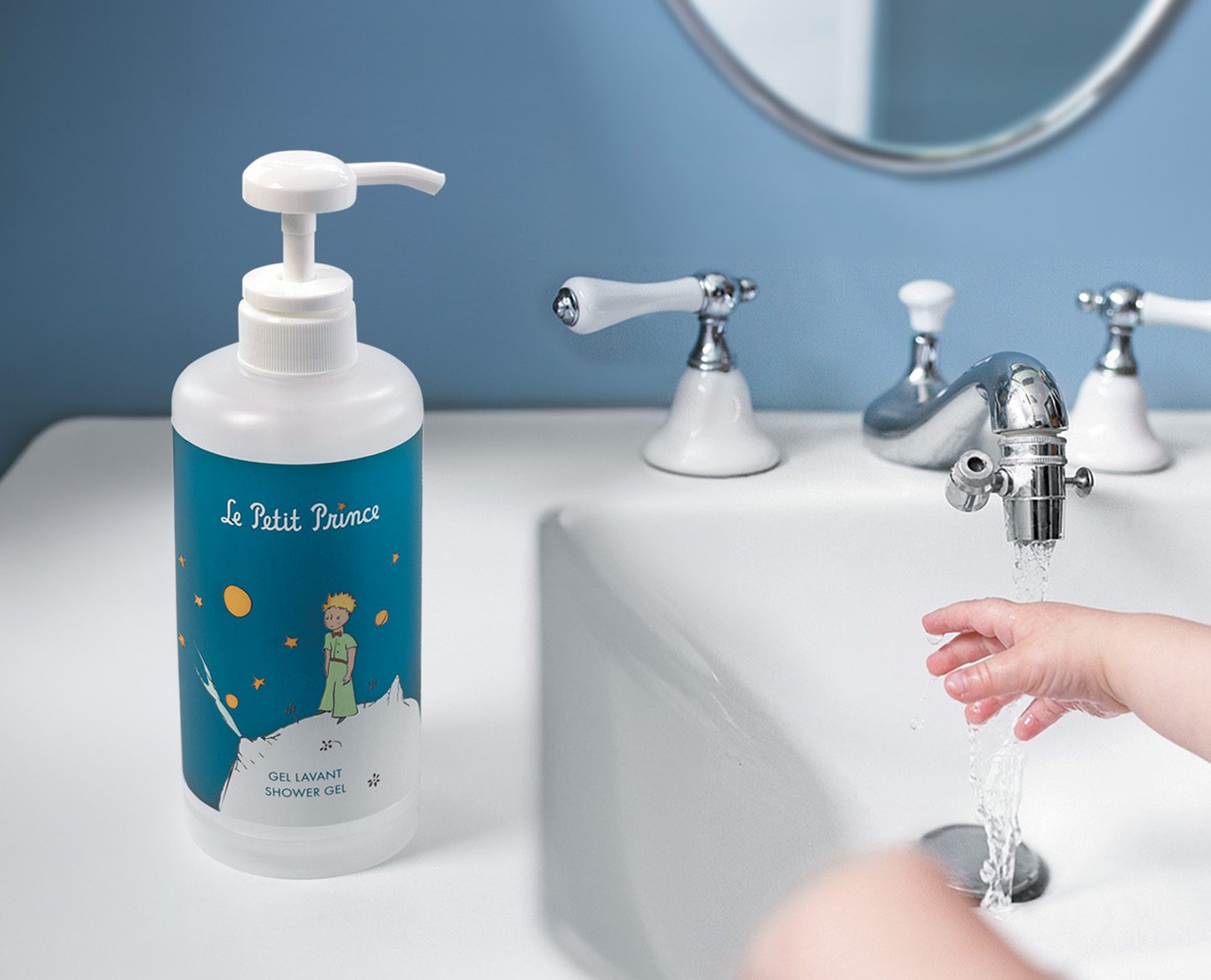 A bottle of "Le Petit Prince" shower gel sits on a washbasin beside a running faucet, while a child's hand reaches toward the water.
