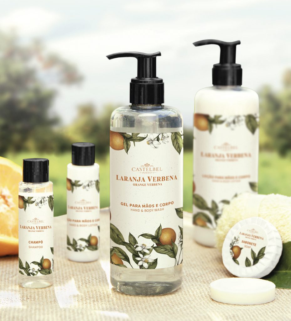 A collection of personal care products labeled "Laranja Verbena" (Orange Verbena), including a large hand and body wash bottle, a shampoo bottle, and a body scrub, all adorned with floral designs.