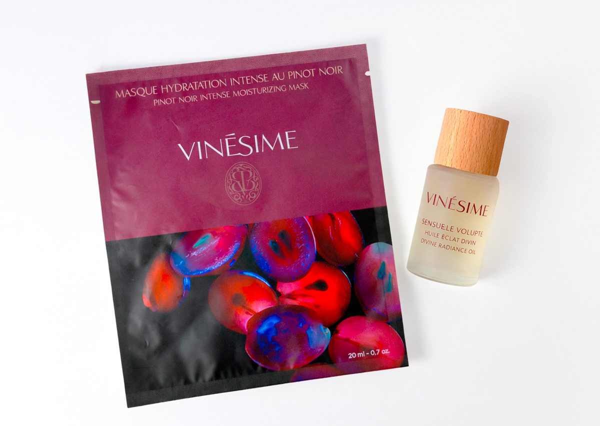 A pouch of Vinésime Pinot Noir Intense Moisturizing Mask alongside a bottle of Vinésime Sensuelle Volupté Radiance Oil, both featuring vibrant, colorful packaging.