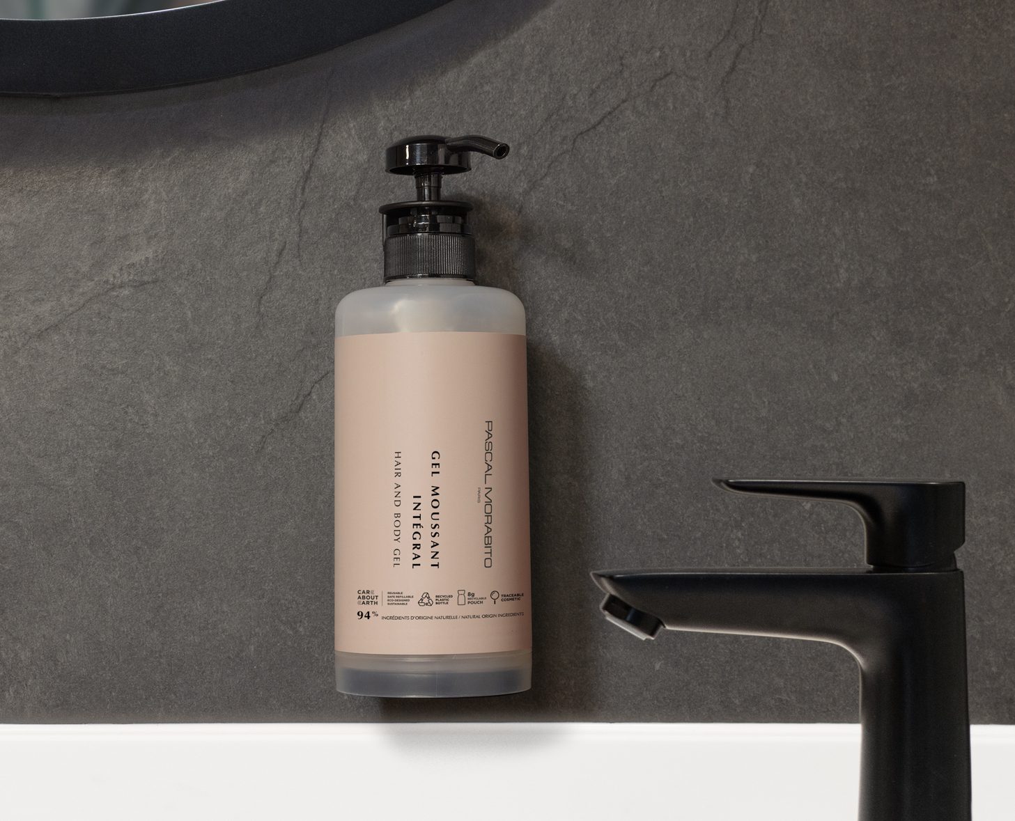 A beige pump bottle labeled "Gel Moisturizer" hangs on a dark stone wall, next to a sleek black faucet.