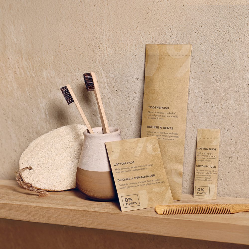 A wooden toothbrush and a cotton pad packaging sit alongside a clay pot and a natural sponge on a shelf, highlighting eco-friendly personal care products.