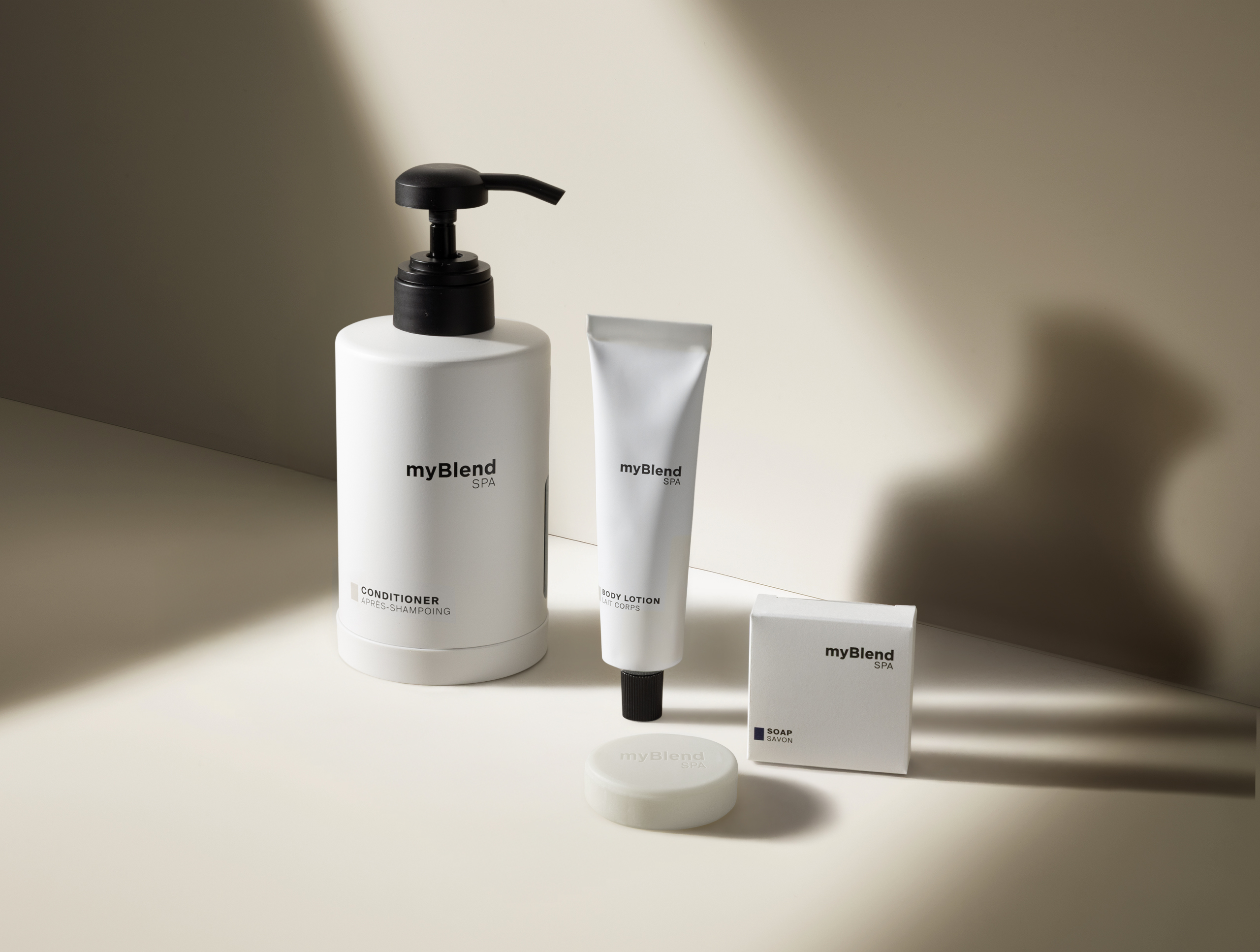 Minimalistische, weiße myBlend Spa , darunter Haarspülung, Körperlotion und Seife, präsentiert vor einem neutralen Hintergrund mit sanften Schatten.