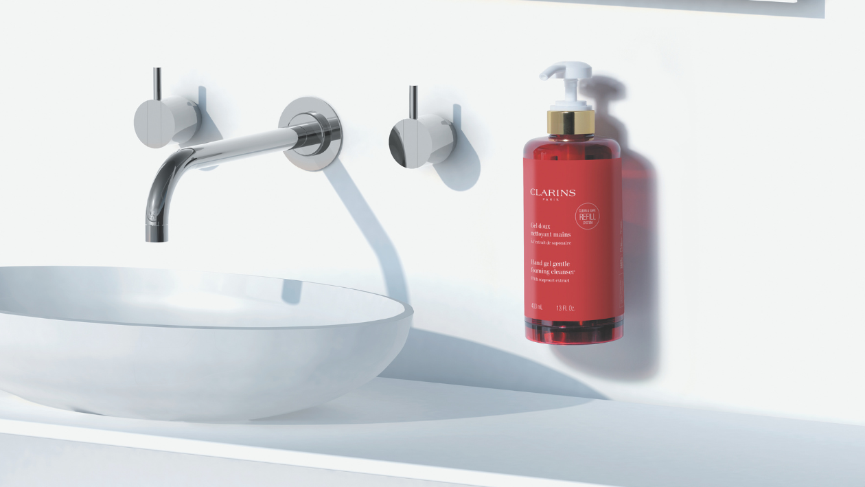 Clarins hand wash bottle mounted beside a modern sink, displayed in a clean, minimalist bathroom setting.