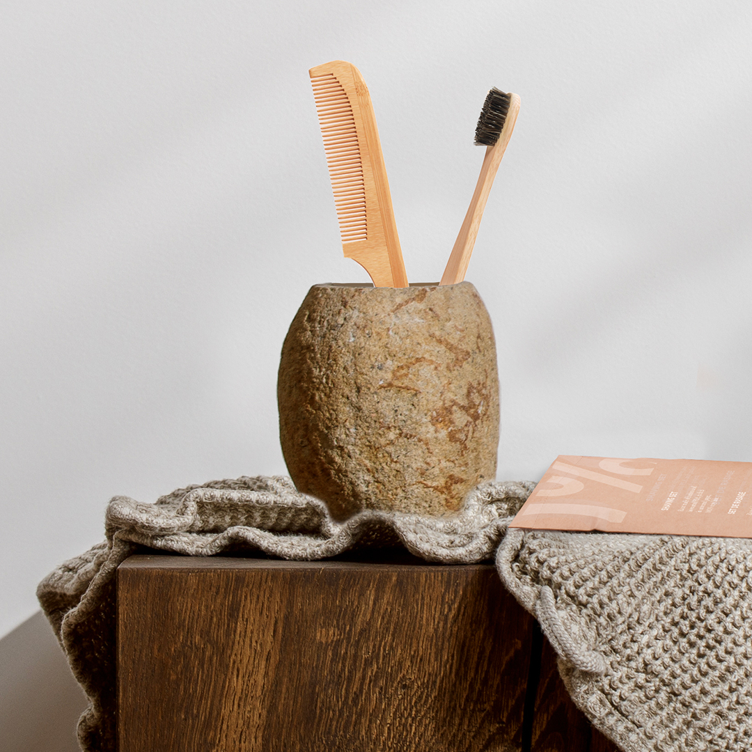 Eco-friendly bamboo toothbrush and wooden comb in a stone cup on a wooden surface with natural fabric