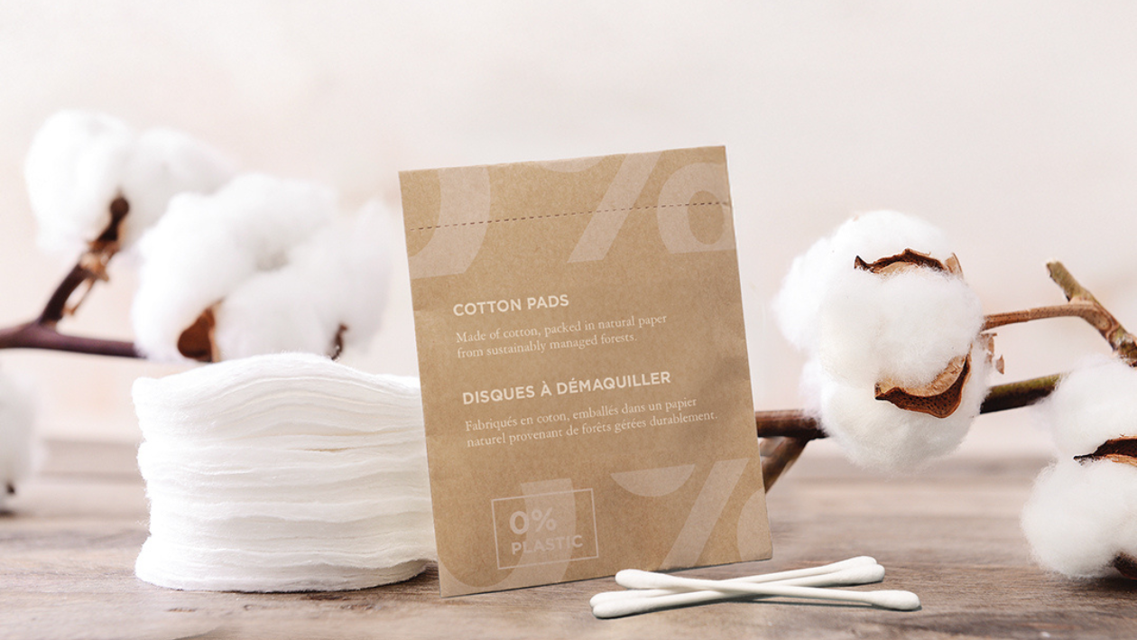 Eco-friendly cotton pads and cotton swabs with natural packaging labeled 0% plastic, displayed with cotton flowers