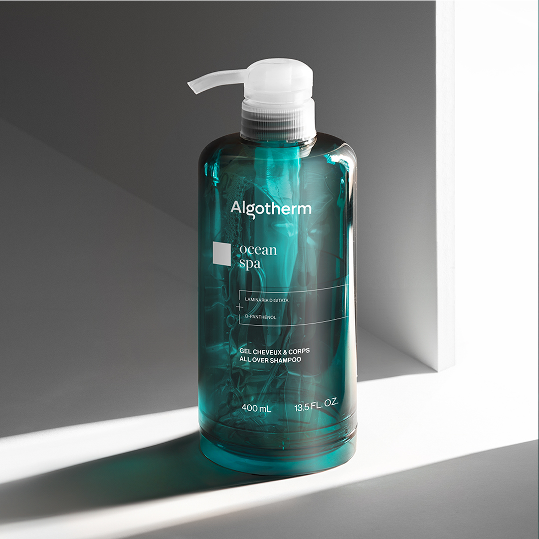 Algotherm Ocean Spa all-over shampoo in a transparent teal pump bottle, displayed in soft light against a minimalist background