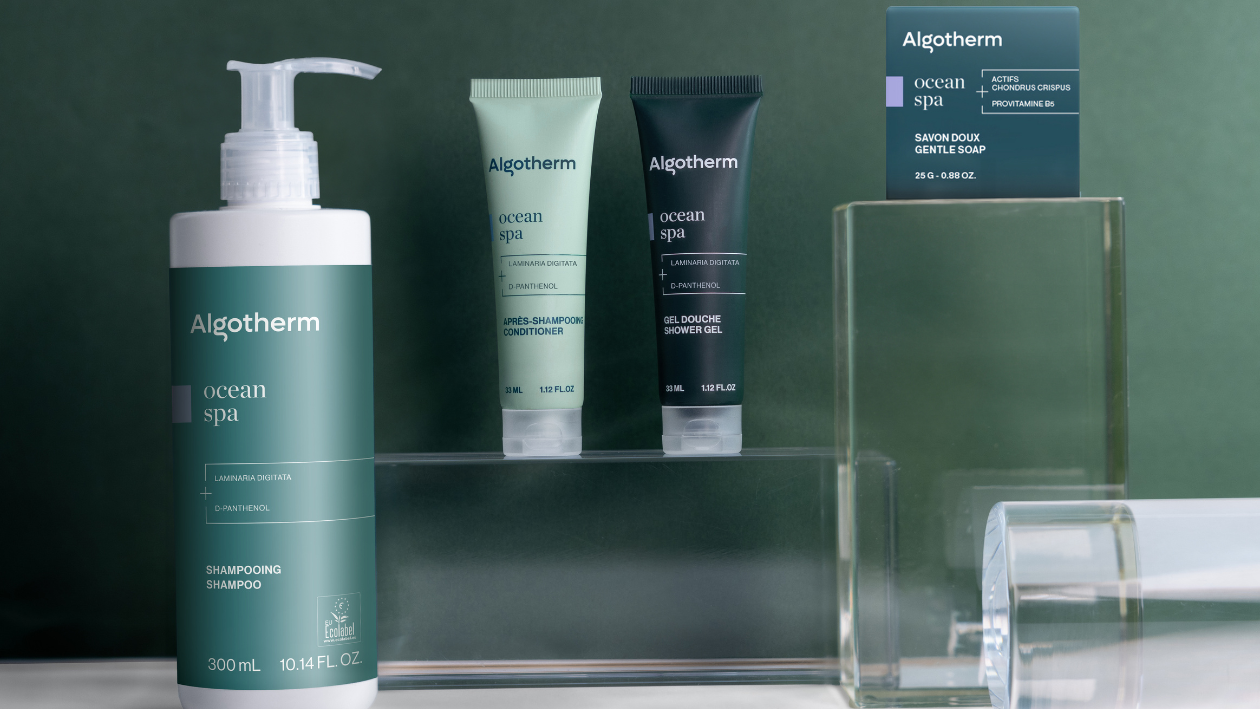 Algotherm Ocean Spa product range including shampoo, conditioner, shower gel, and soap displayed on glass stands with a green background