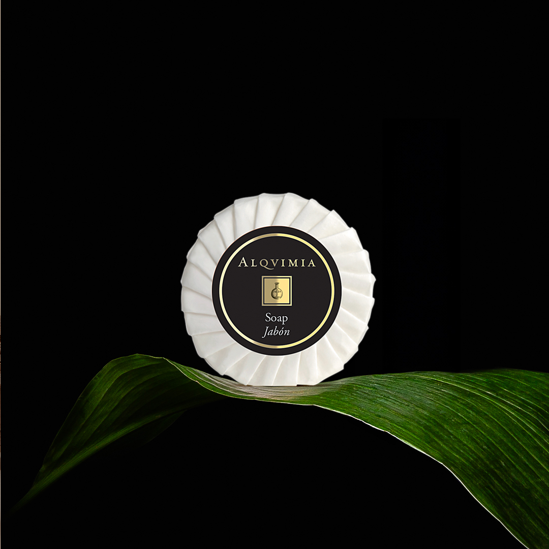 Alqvimia soap in pleated packaging placed on a green leaf against a black background