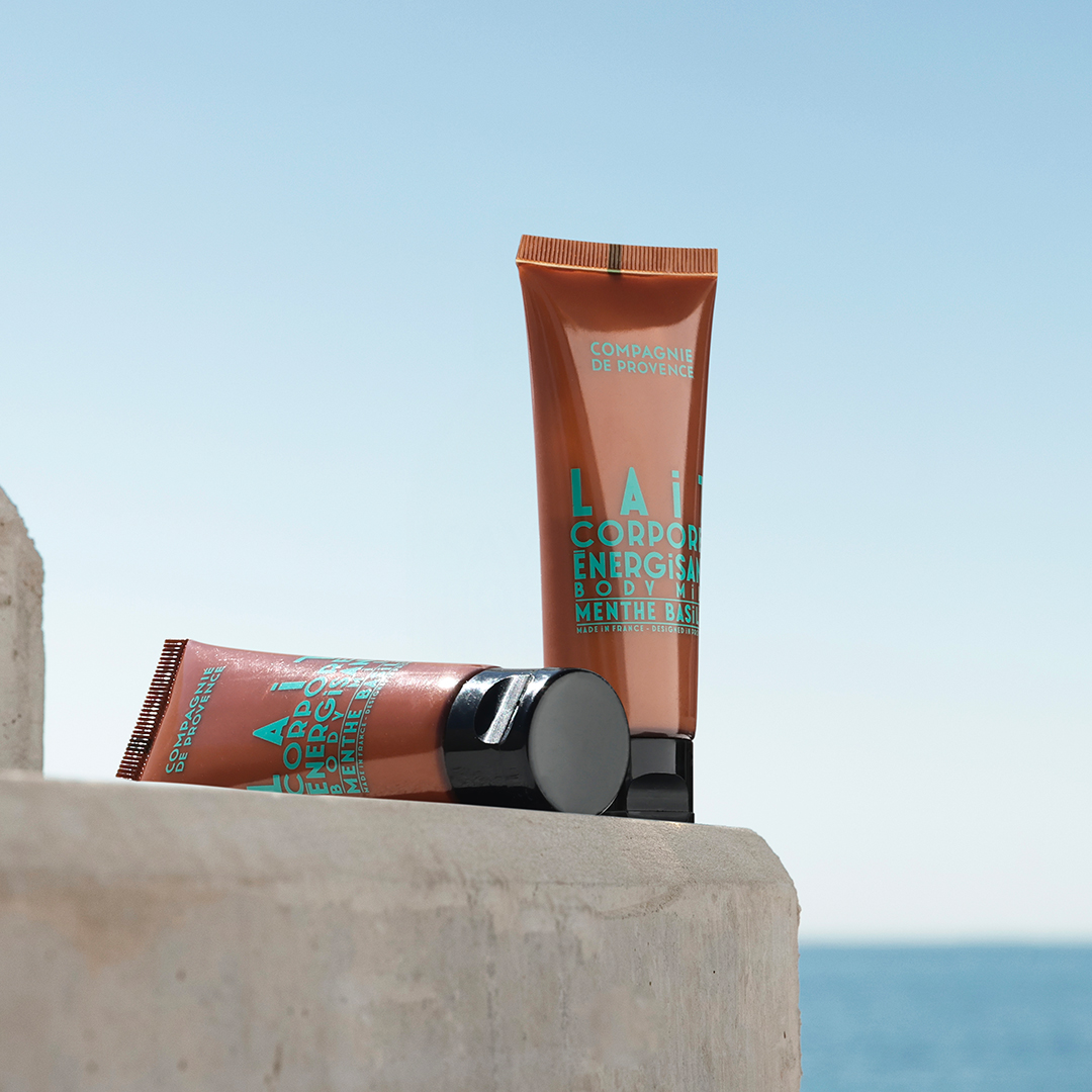 Compagnie de Provence body lotion tubes displayed on a stone surface with a sea view in the background