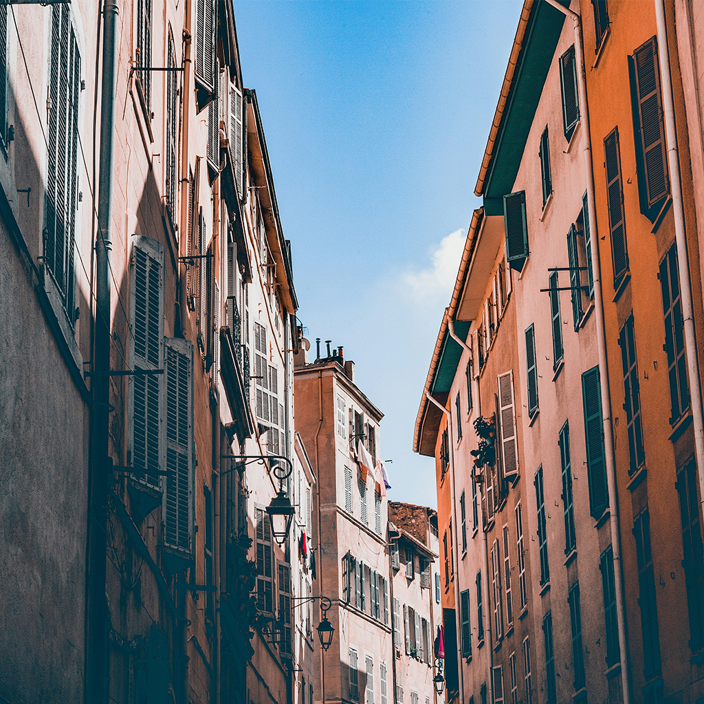 Narrow street lined with pastel-colored buildings and shuttered windows under a blue sky in a Mediterranean town