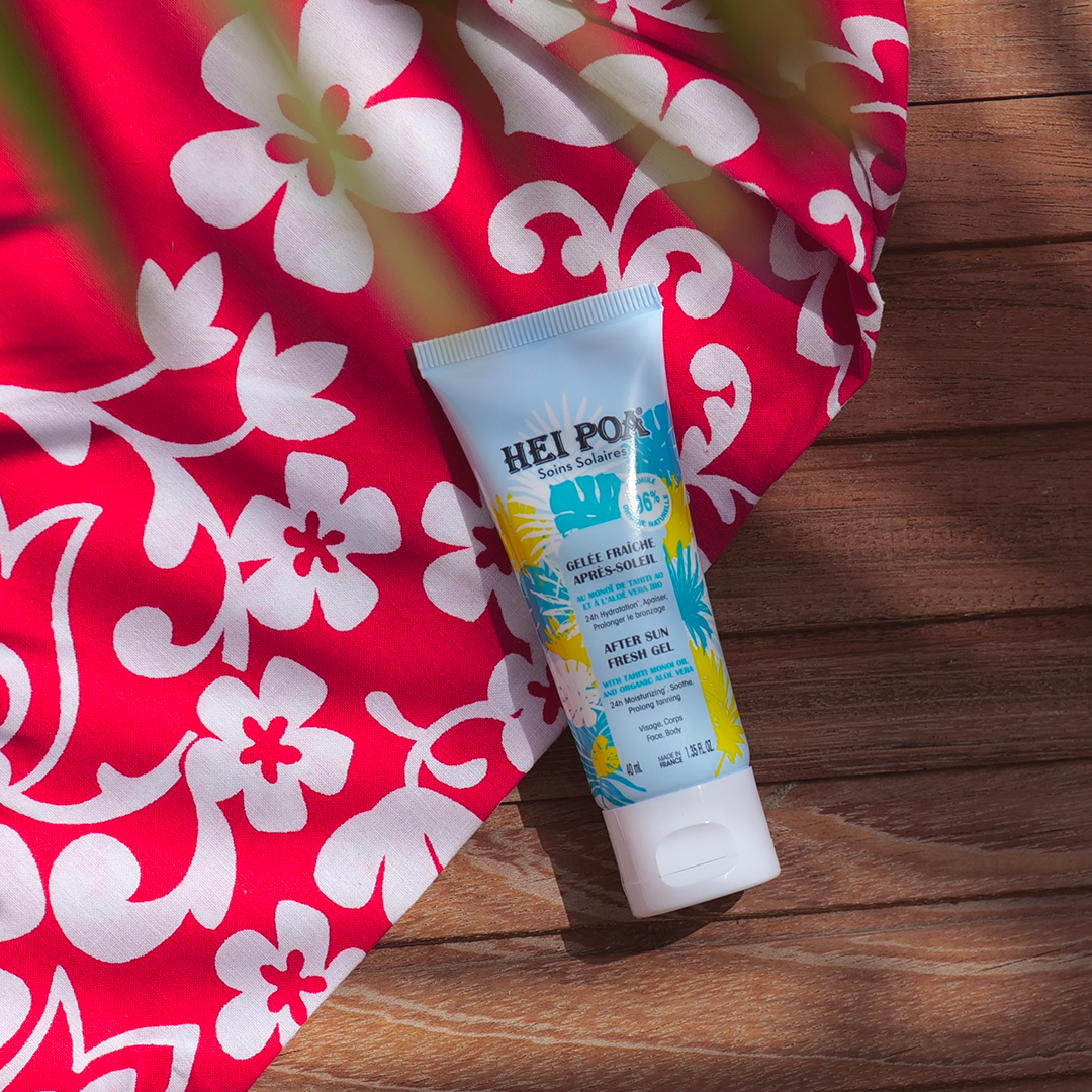 Hei Poa after-sun fresh gel tube placed on a wooden surface next to a red floral fabric