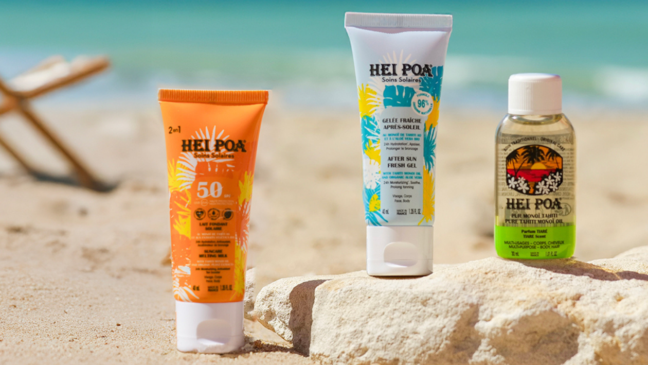 Hei Poa sun care products including SPF 50 sunscreen, after-sun gel, and monoi oil displayed on sand at the beach