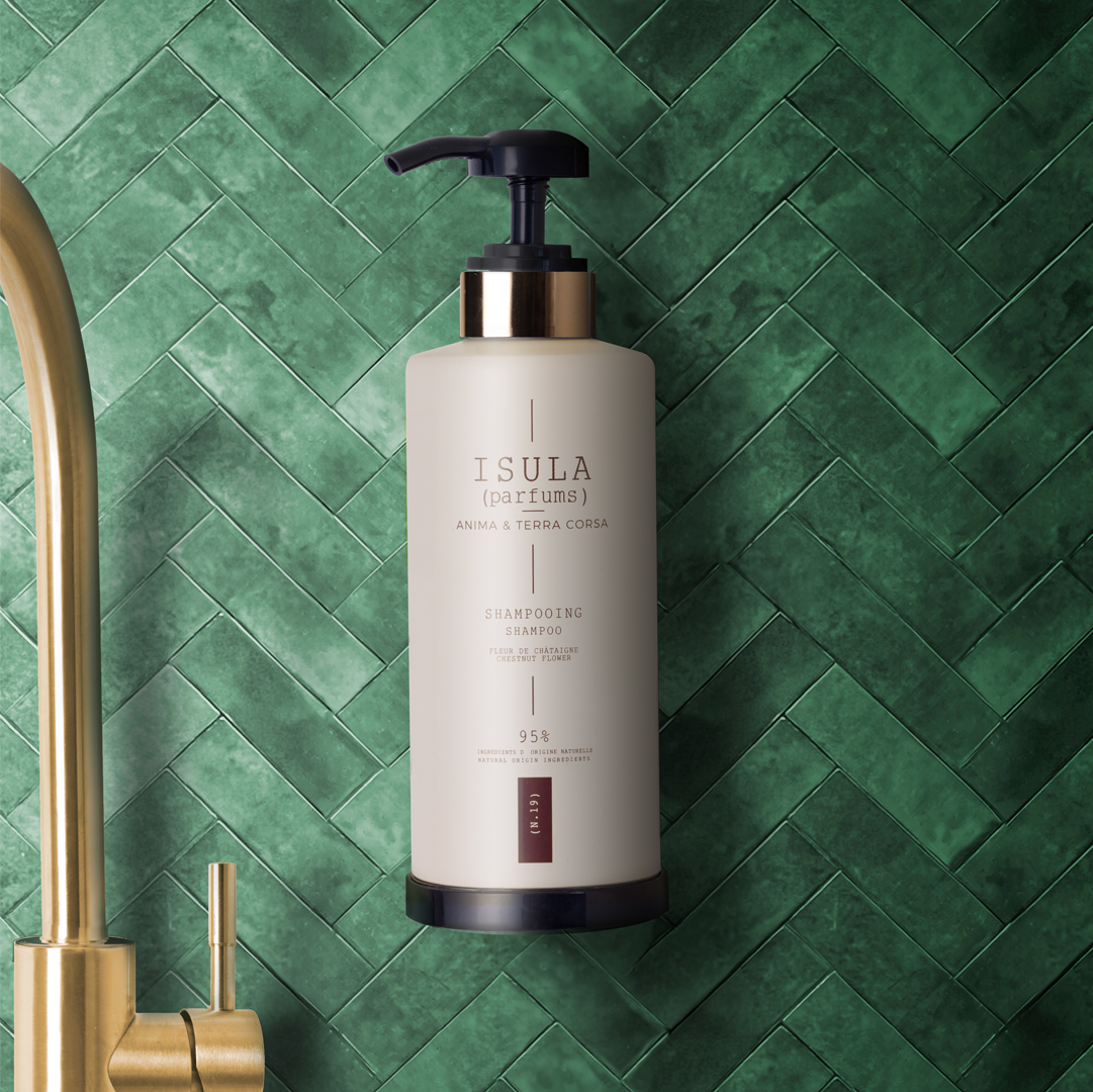 Isula Parfums shampoo bottle with pump mounted on a green tiled wall near a faucet