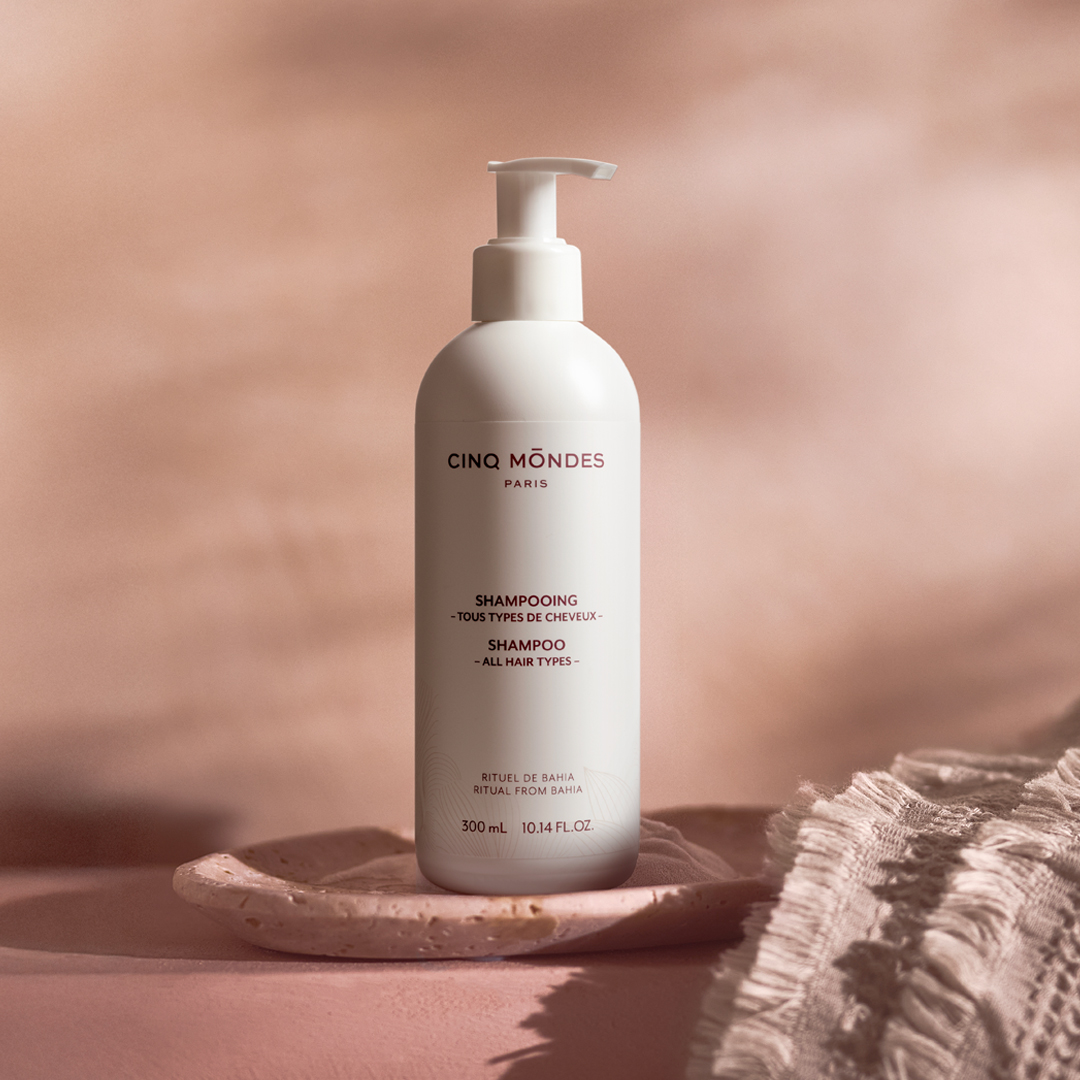 Cinq Mondes Paris shampoo bottle with pump dispenser on a ceramic dish, set against a soft beige background