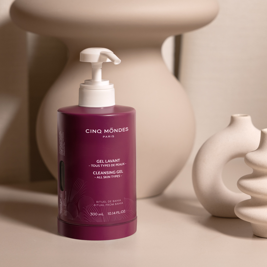 Cinq Mondes Paris cleansing gel bottle with pump dispenser, burgundy packaging, displayed with neutral-toned ceramic decor