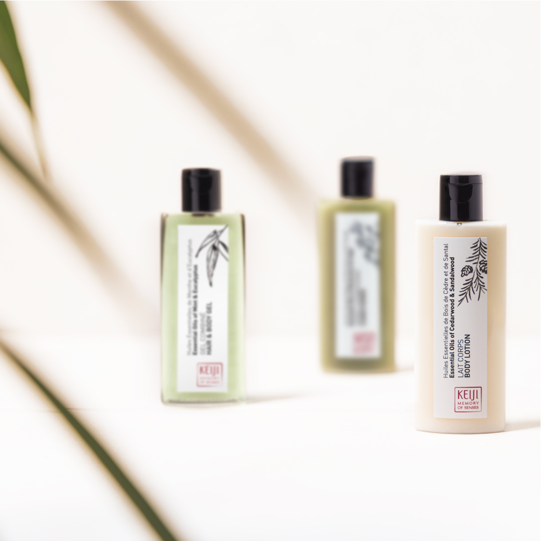 Keiji Memory of Senses hair and body gel in a green transparent bottle with black pump, placed on a white surface with strong sunlight casting shadows, highlighting a fresh, botanical-inspired design.