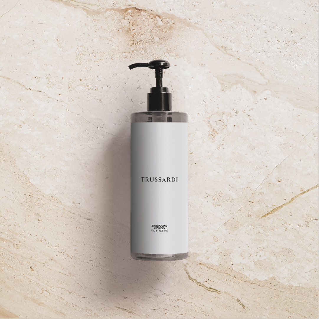 Trussardi shampoo bottle with a black pump centered on a beige marble background, featuring a minimalist white label and soft shadows emphasizing a clean, elegant design.