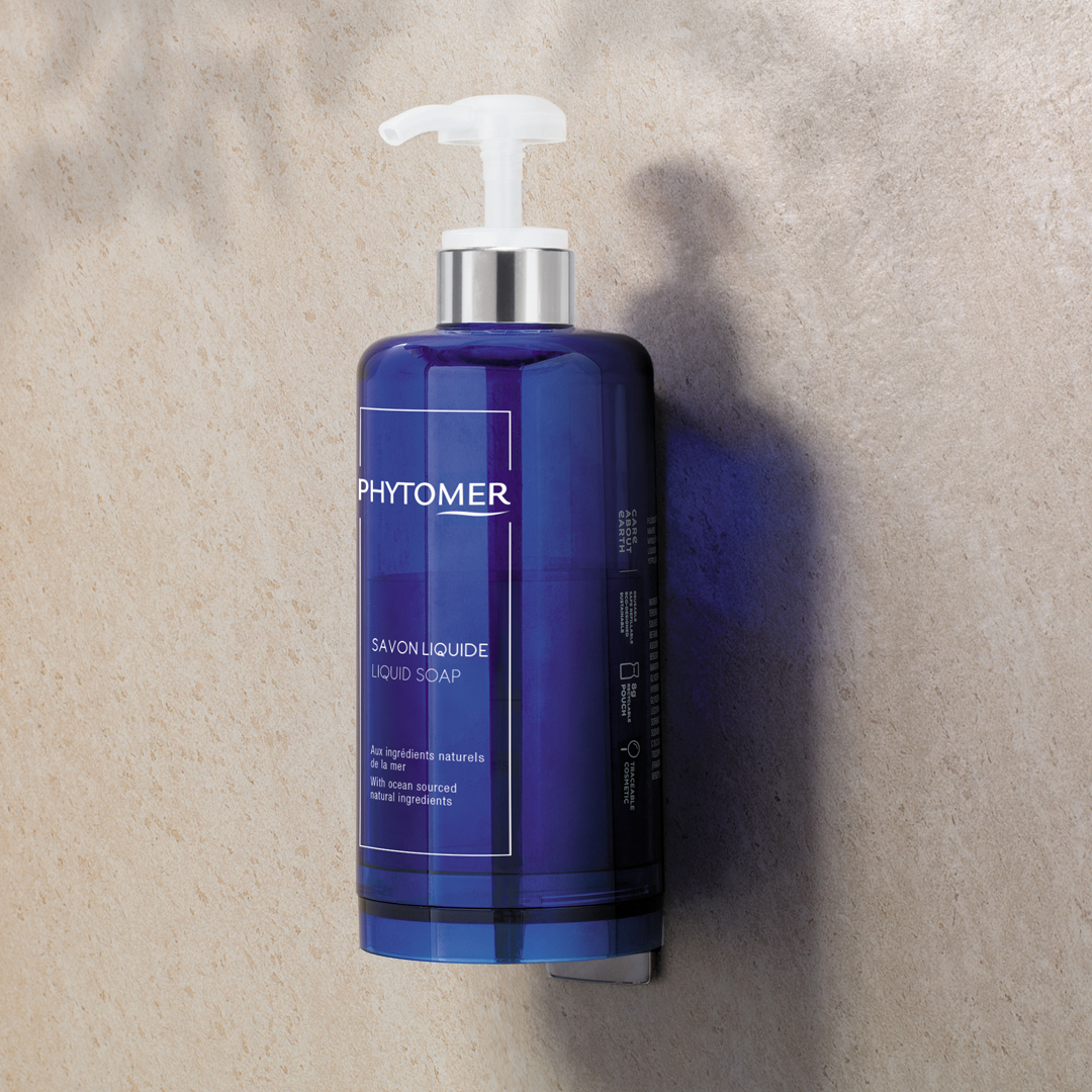 Phytomer Flacon de savon liquide posé sur un mur de pierre, mis en valeur par la lumière naturelle et les ombres.