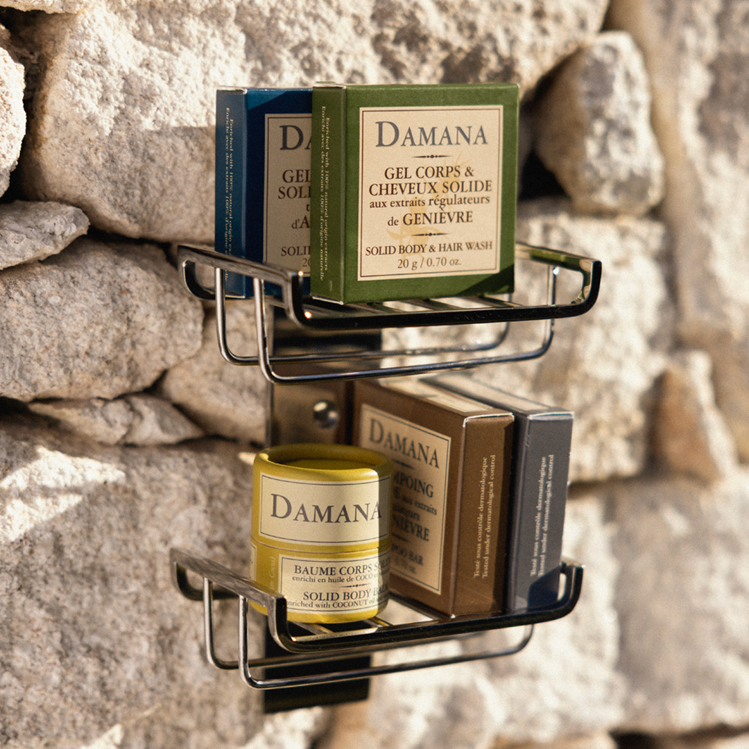 Wall-mounted shelves holding Damana solid skincare products, including boxed solid body and hair wash and a solid body balm, set against a textured stone wall.
