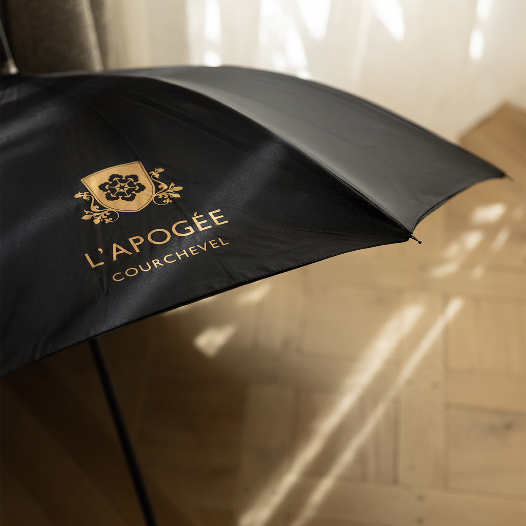 Branded black umbrella displayed indoors on a wooden floor.