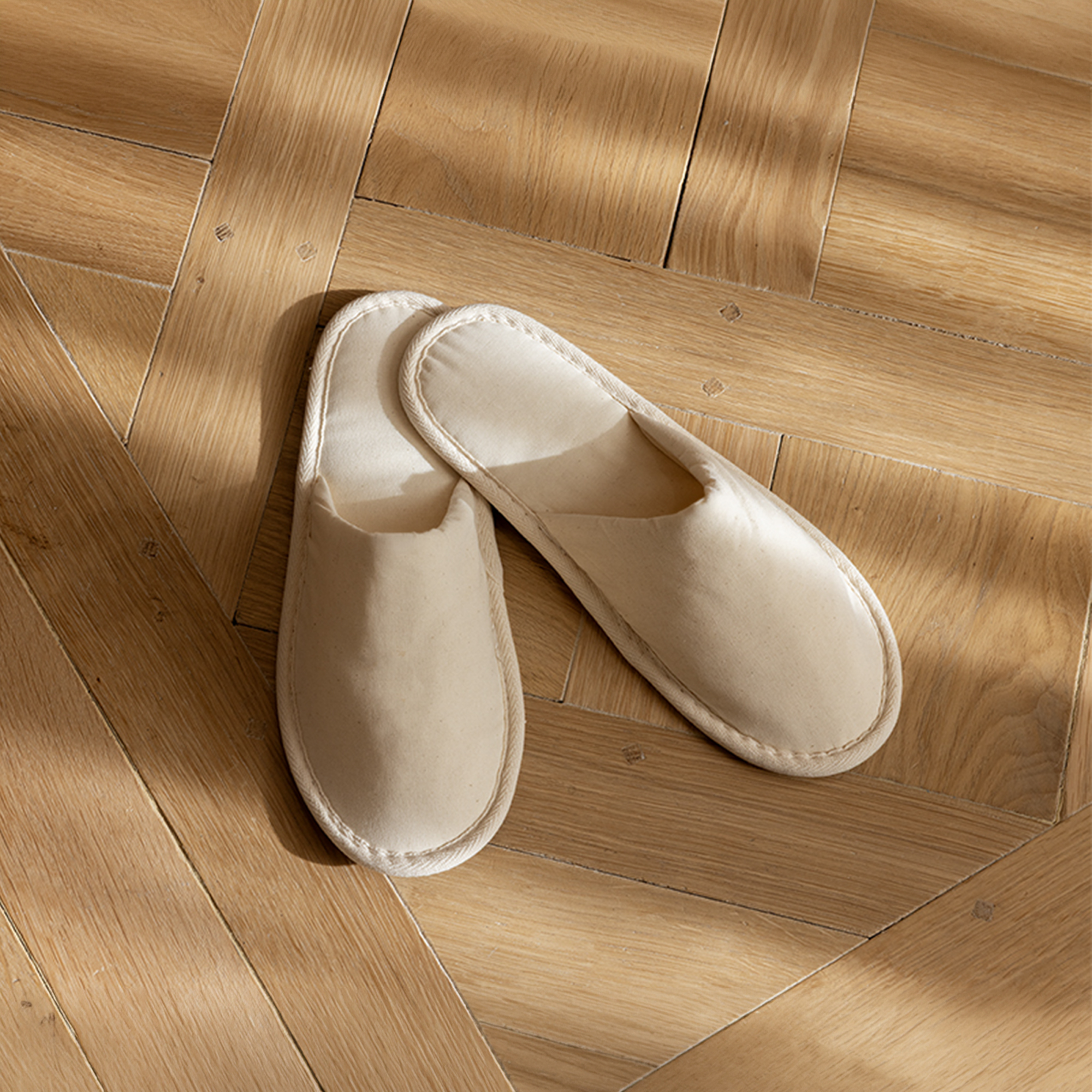 Pair of hotel slippers placed on a wooden parquet floor.