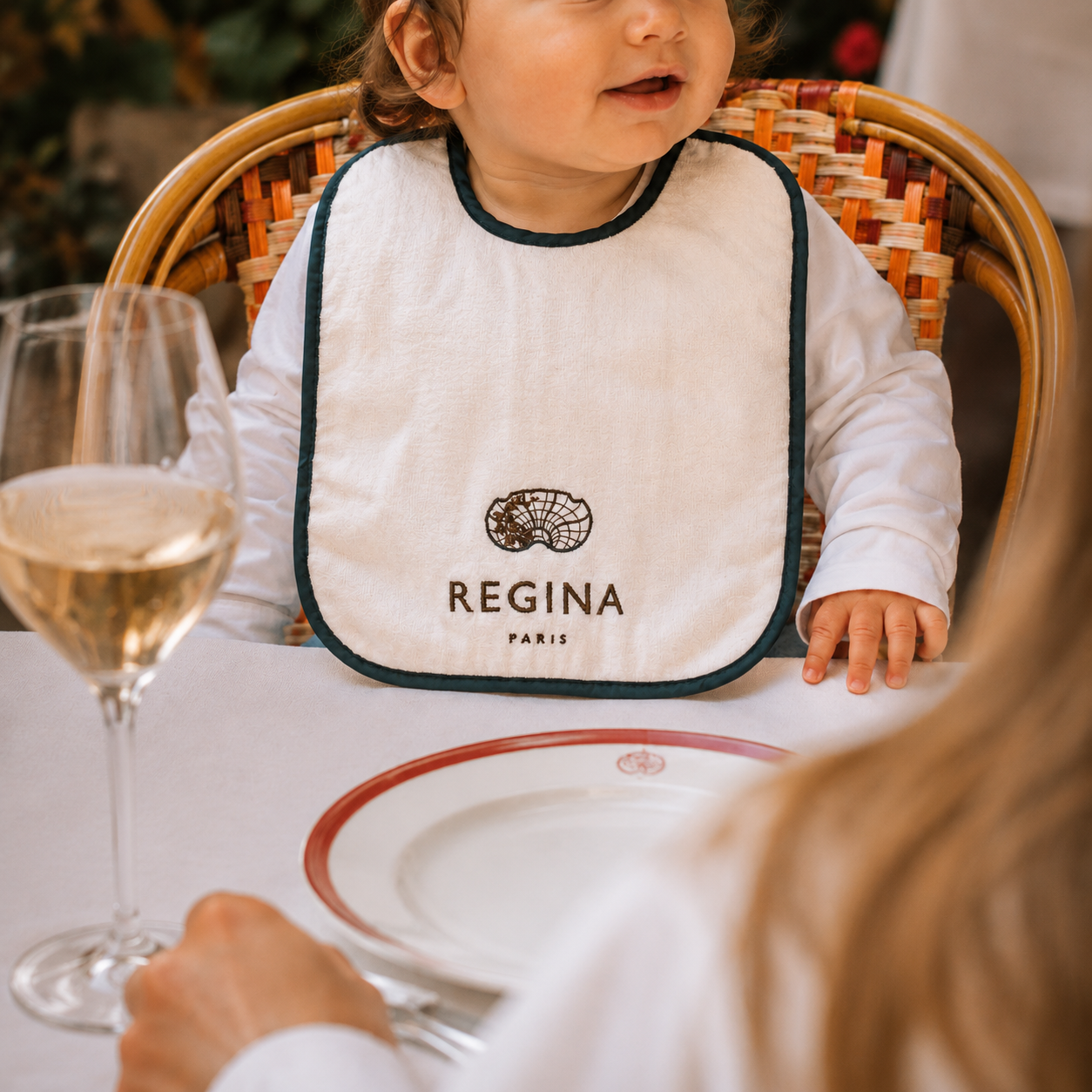 Branded baby bib worn by a child at a dining table.