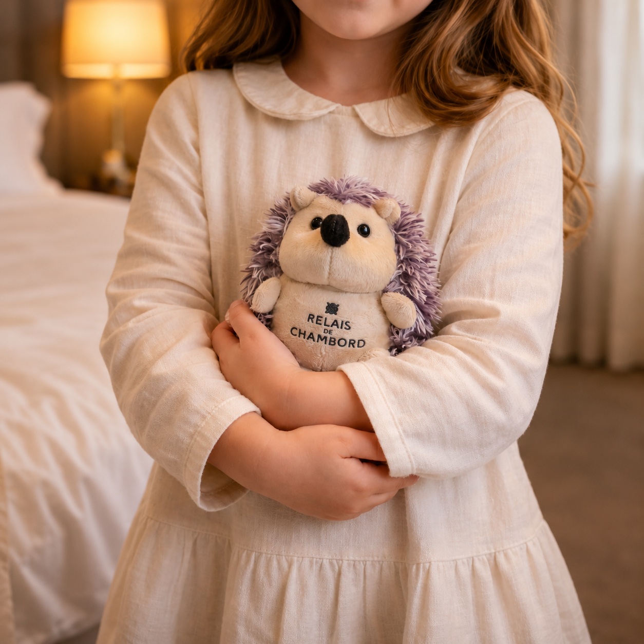Child holding a branded hedgehog plush toy in a hotel room.